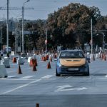 Faceless rider driving classic sport car on asphalt track with traffic cones during race