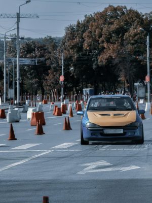 Faceless rider driving classic sport car on asphalt track with traffic cones during race